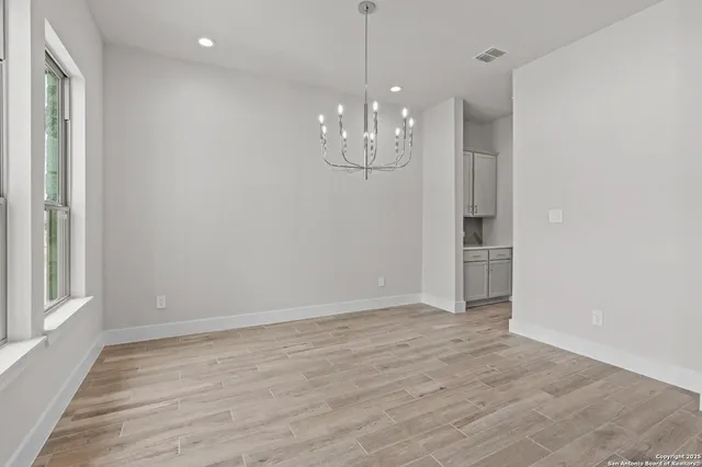 a view of an empty room with wooden floor and kitchen view