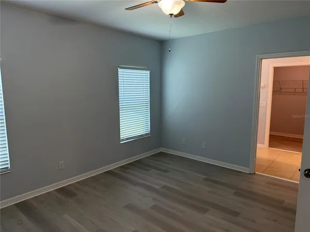 an empty room with wooden floor chandelier fan and windows
