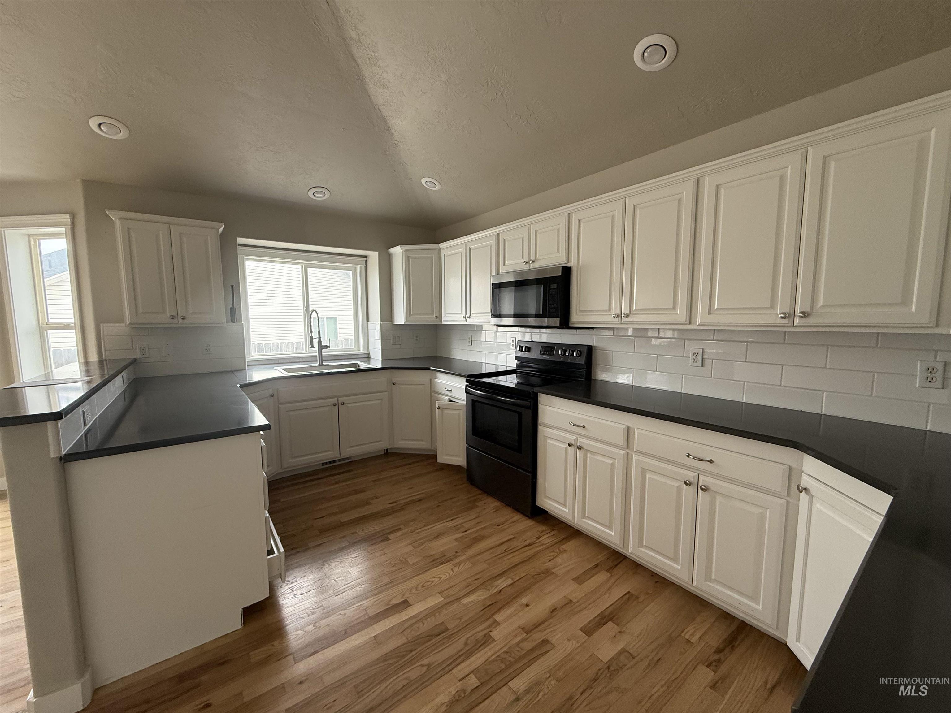 538 Morning Sun Drive Nampa, ID 83686 - Photo 8 of 28 Kitchen with white cabinets, black range with electric cooktop, backsplash, stainless steel microwave, and light wood-style floors