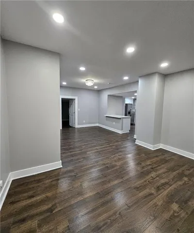 an empty room with wooden floor kitchen view and a window