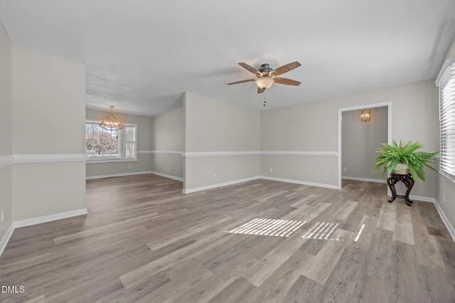 an empty room with wooden floor chandelier and windows