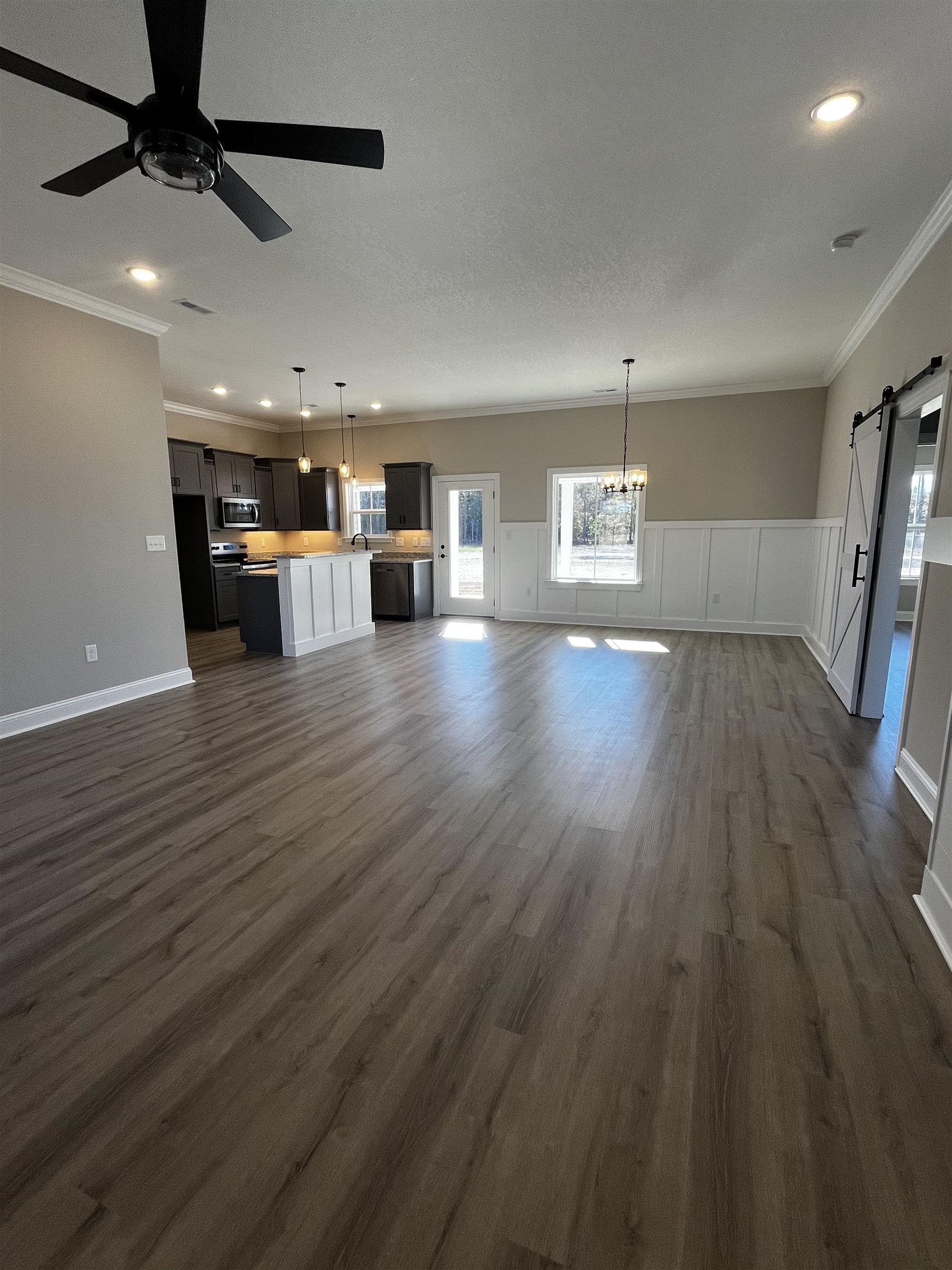 3436 Asbury Road Aynor, SC 29511 - Photo 2 of 9 Unfurnished living room with a barn door, crown molding, a decorative wall, dark wood finished floors, and wainscoting