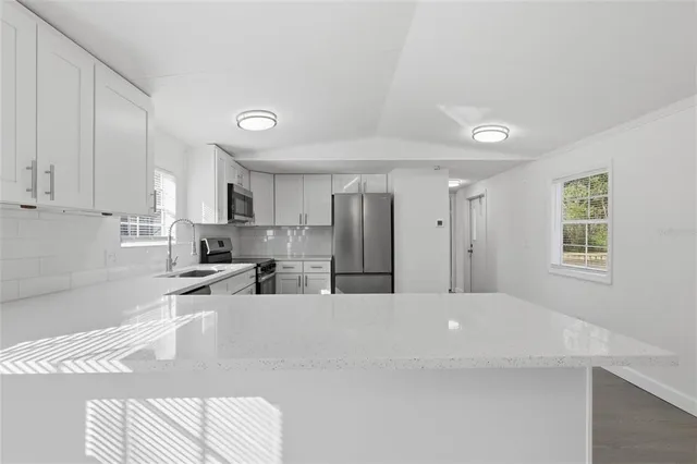 a large white kitchen with kitchen island a sink stainless steel appliances and cabinets