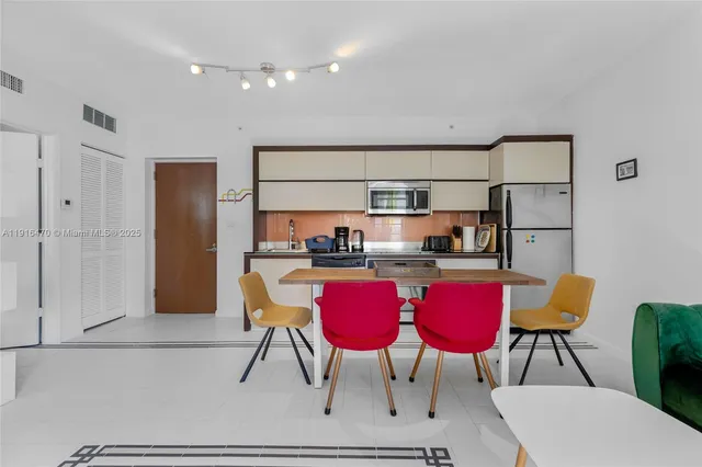 a kitchen with stainless steel appliances kitchen island granite countertop a dining table chairs and refrigerator