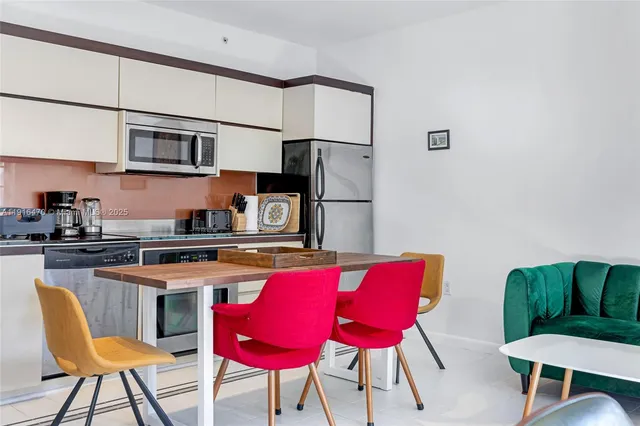 a kitchen with stainless steel appliances granite countertop a dining table chairs refrigerator and sink