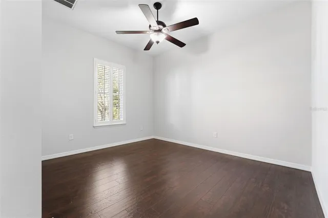 an empty room with wooden floor ceiling fan and windows