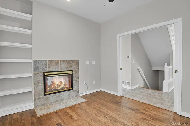 a view of an empty room with wooden floor fire place and windows