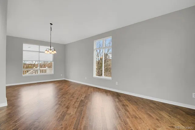 an empty room with wooden floor chandelier and windows