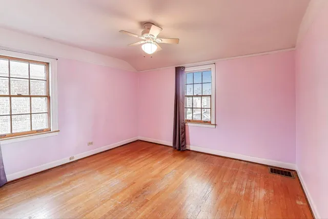 an empty room with wooden floor chandelier fan and windows