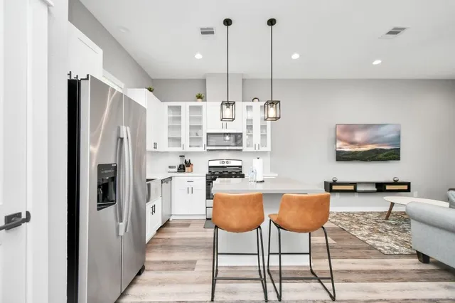 a kitchen with stainless steel appliances kitchen island granite countertop a refrigerator a stove a oven with white cabinets and chairs