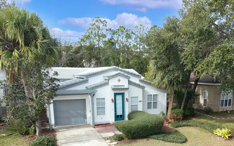 a view of a white house next to a yard with plants and trees
