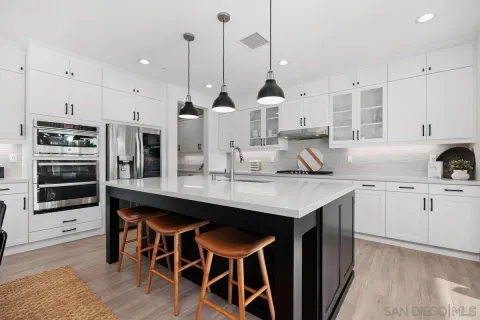 a kitchen with stainless steel appliances kitchen island granite countertop a table chairs in it and white cabinets