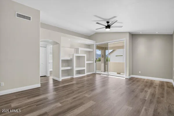 an empty room with wooden floor ceiling fan and windows