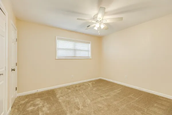 an empty room with a chandelier fan and windows