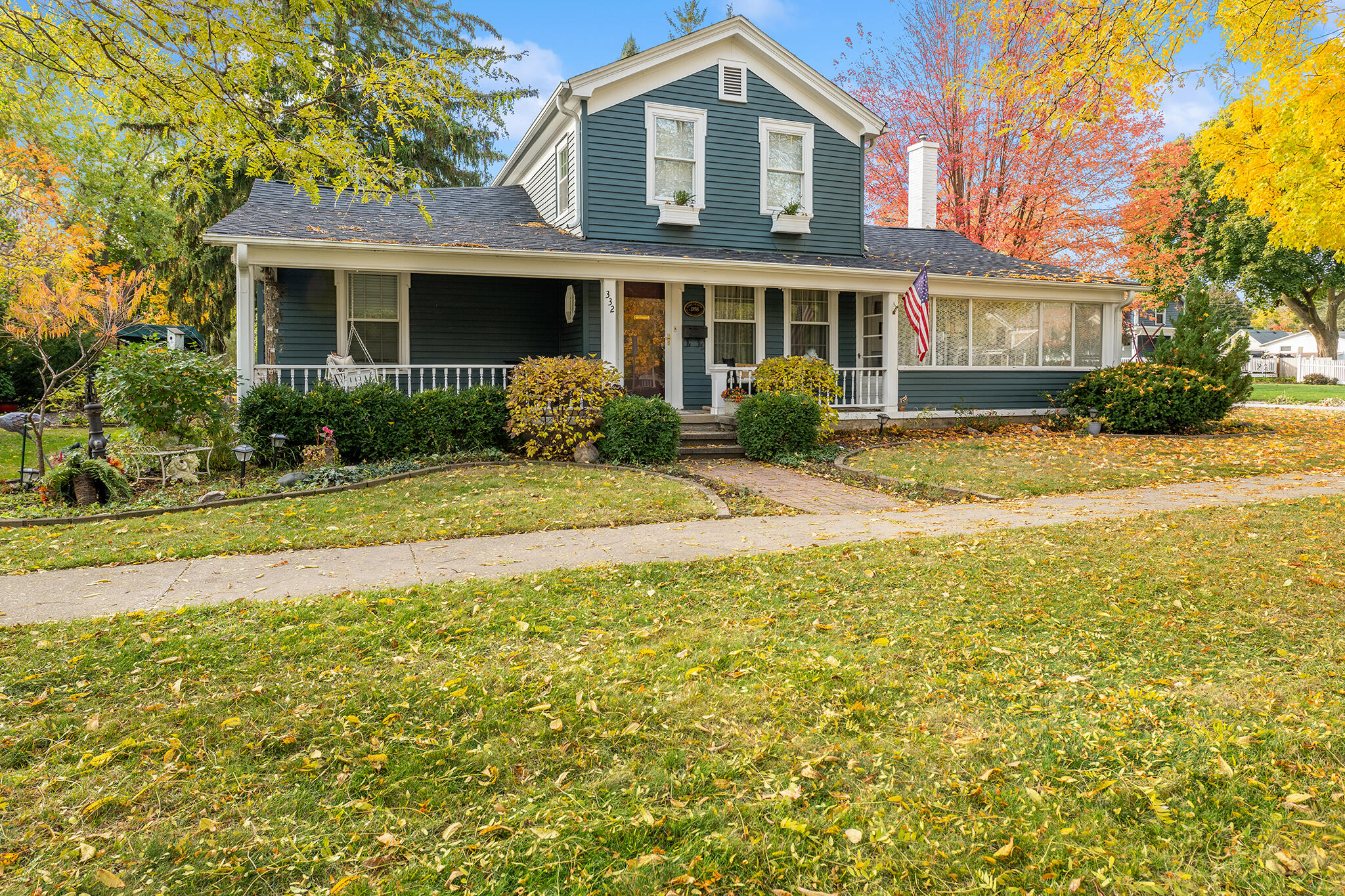 Charming two-story façade with classic siding, wide front porch, and beautifully maintained landscaping framed by vibrant autumn foliage.