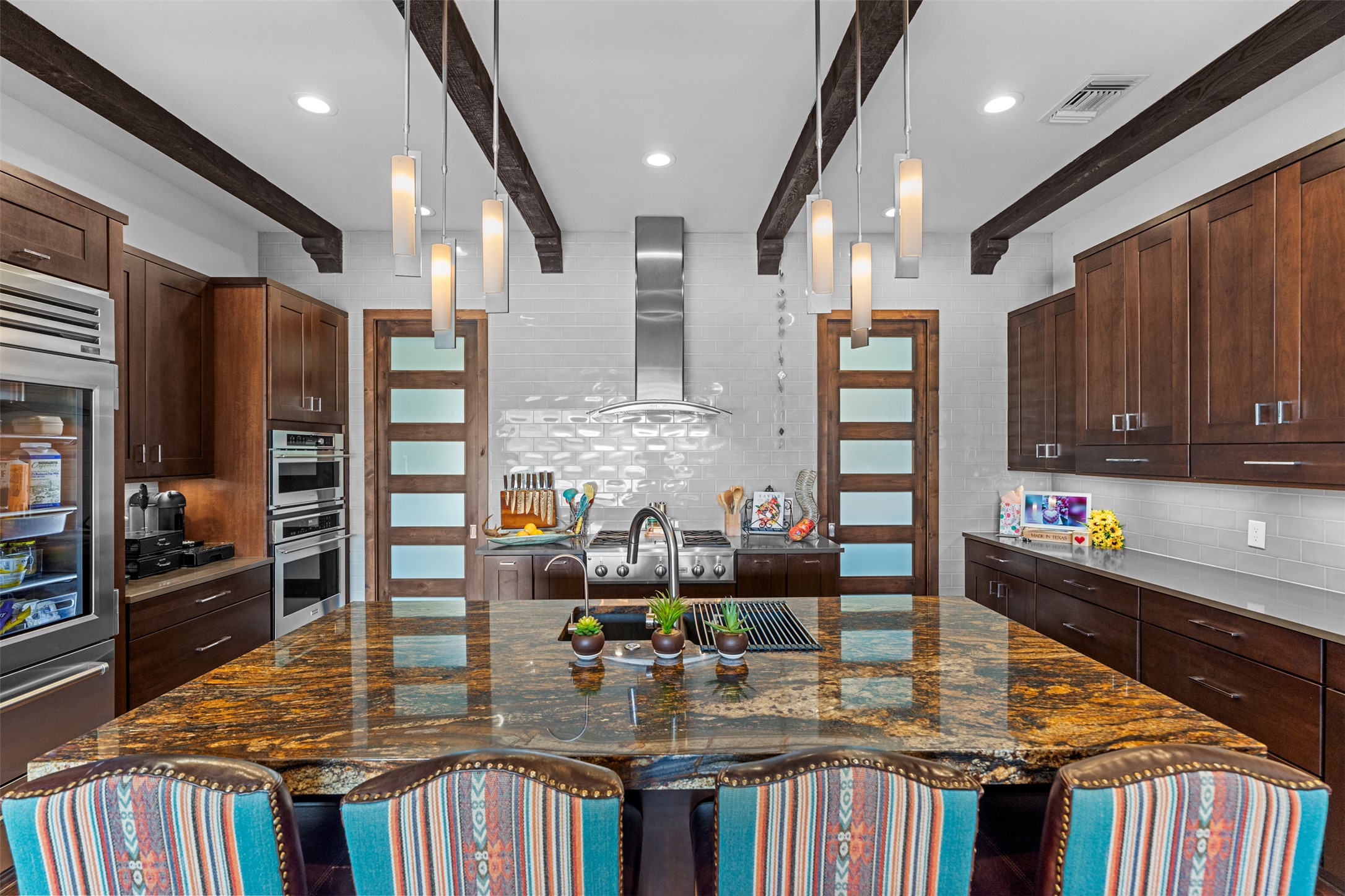 421 Rolling Hills Road Blanco, TX 78606 - Photo 11 of 40 The kitchen features a large island with a patterned granite countertop, dark wood cabinetry, and stainless steel appliances.