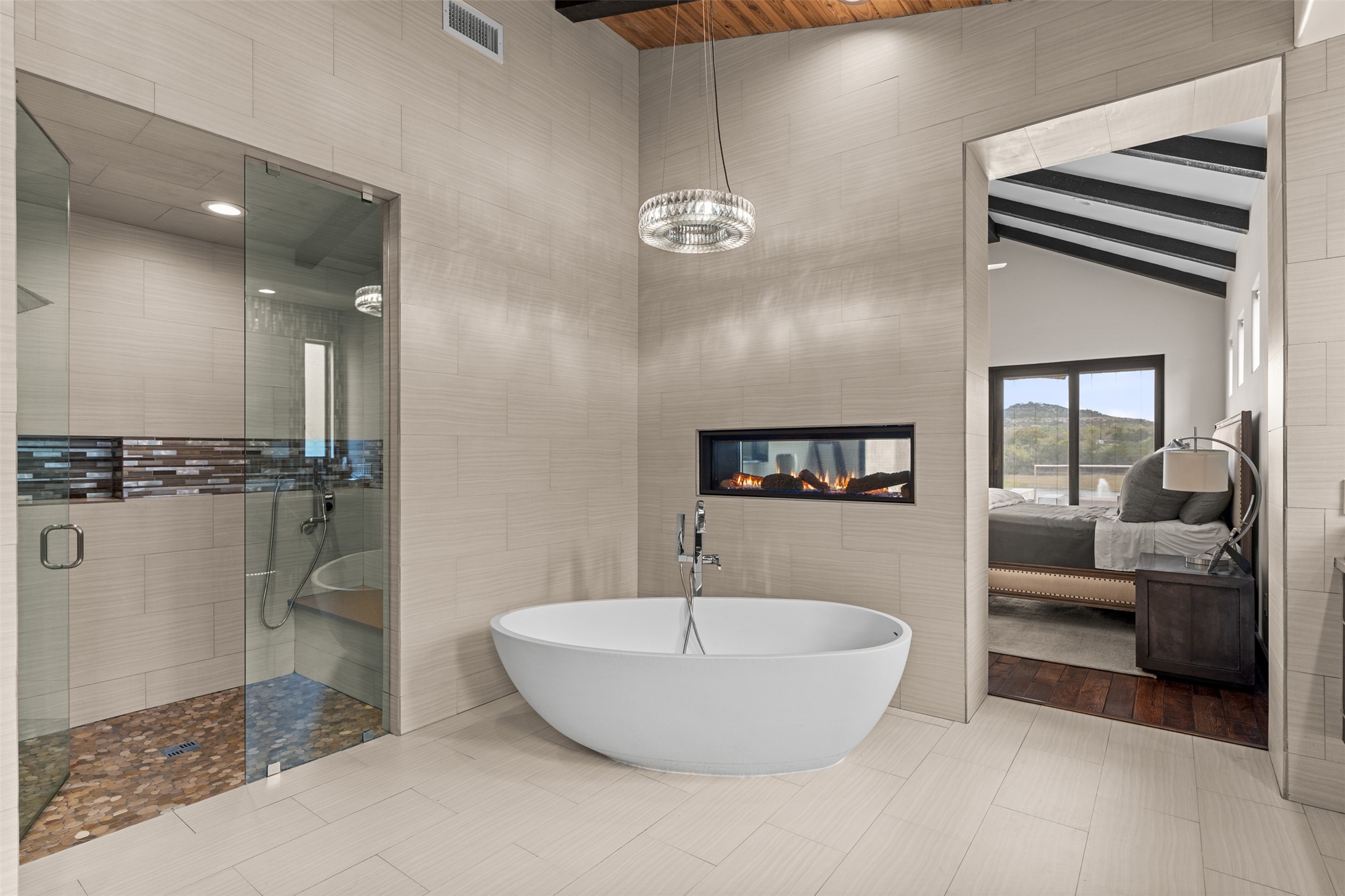 421 Rolling Hills Road Blanco, TX 78606 - Photo 15 of 40 This bathroom features a freestanding soaking tub, a walk-in shower with a glass enclosure, and a modern linear fireplace.