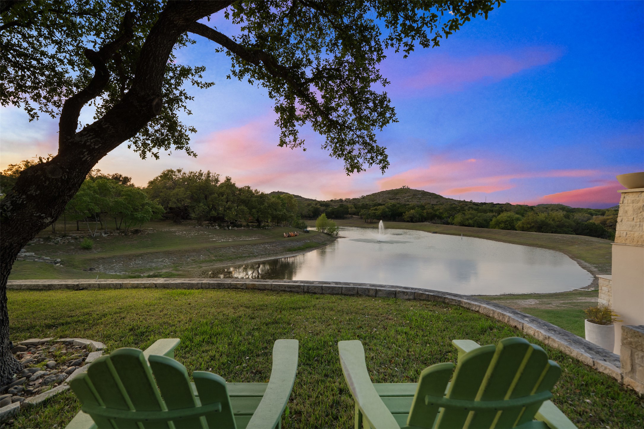 421 Rolling Hills Road Blanco, TX 78606 - Photo 20 of 40 The property features a spacious lawn area with a stone retaining wall, offering scenic views of the private lake and distant hills.