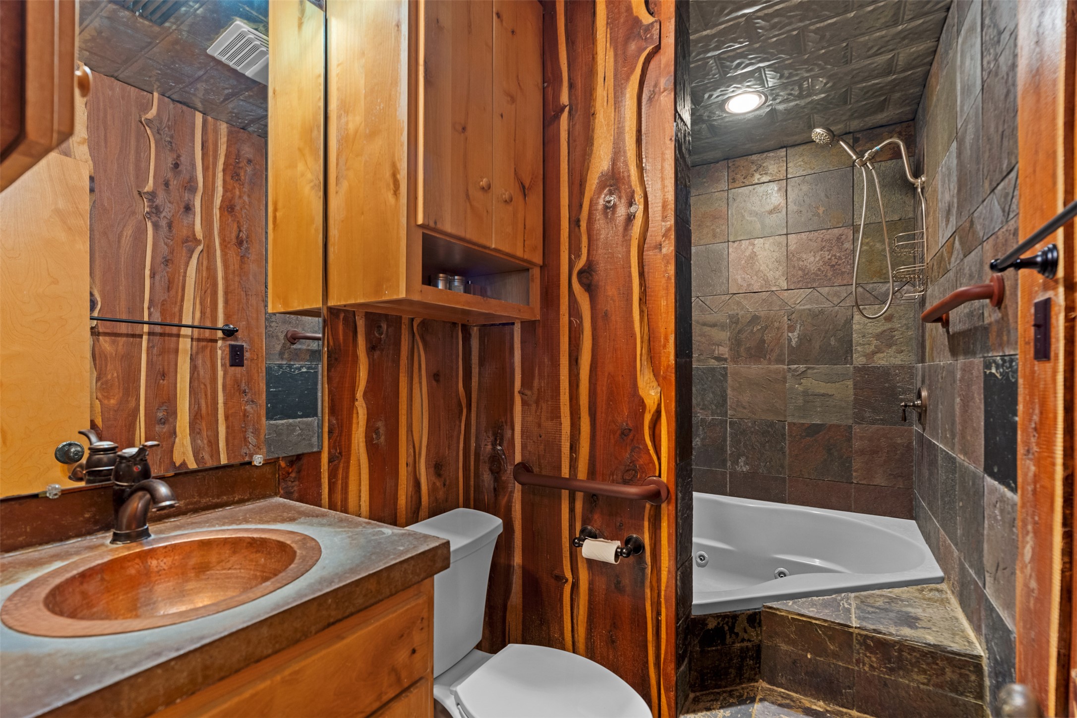 421 Rolling Hills Road Blanco, TX 78606 - Photo 27 of 40 The bathroom features wood paneling, a copper sink, a vanity with storage, and a tiled shower area with a built-in tub.