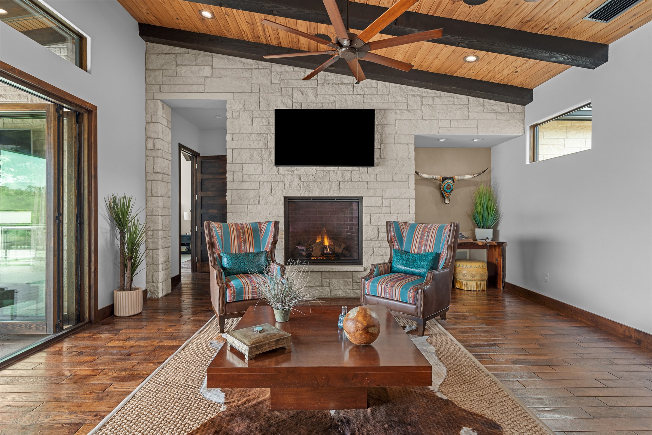 421 Rolling Hills Road Blanco, TX 78606 - Photo 9 of 40 Living area featuring a stone fireplace, hardwood floors, a wood plank ceiling with exposed beams, and sliding glass doors opening up to the patio.