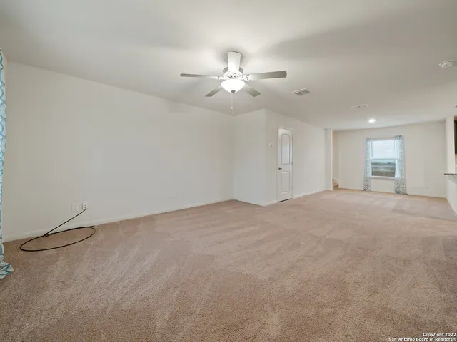 an empty room with chandelier fan and windows