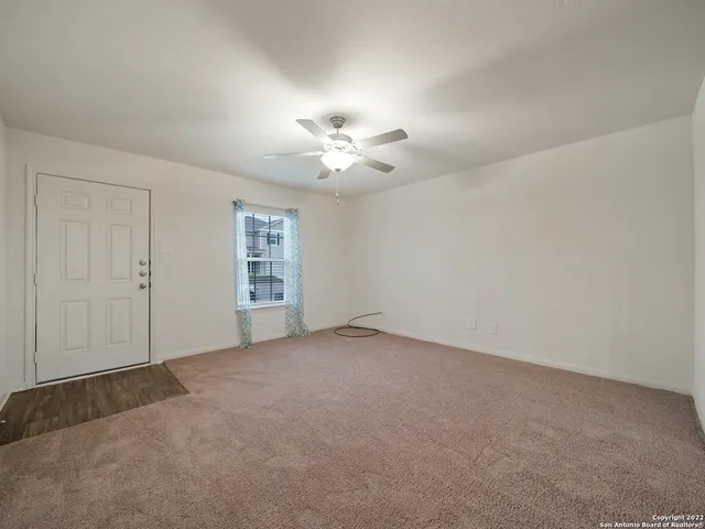 an empty room with chandelier fan and windows