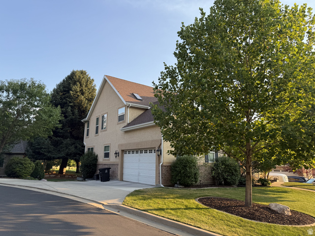 2388 East 850 South Springville, UT 84663 - Photo 5 of 24 Two-story brick residence featuring a peaked roofline with dormer windows, attached two-car garage with paneled door, and mature landscaping including shade trees and manicured foundation plantings