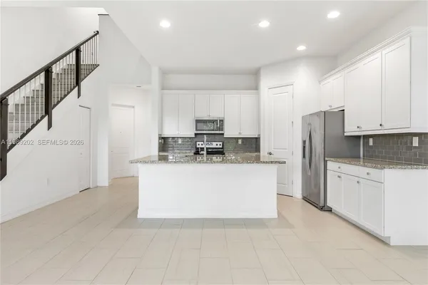 a view of kitchen with stainless steel appliances granite countertop a stove a sink a refrigerator and white cabinets