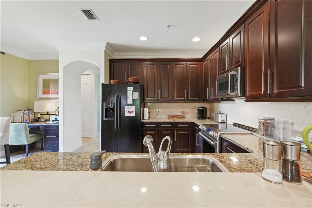 9108 Capistrano Street South, Unit 7401 Naples, FL 34113 - Photo 14 of 44 a kitchen with stainless steel appliances granite countertop a refrigerator a stove and a sink with wooden cabinets