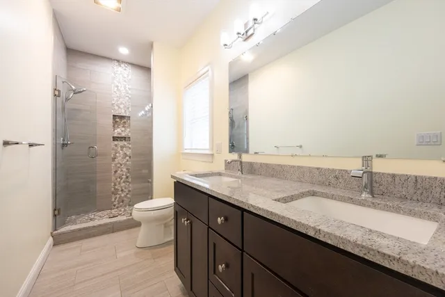 a bathroom with a granite countertop double vanity sink toilet and shower