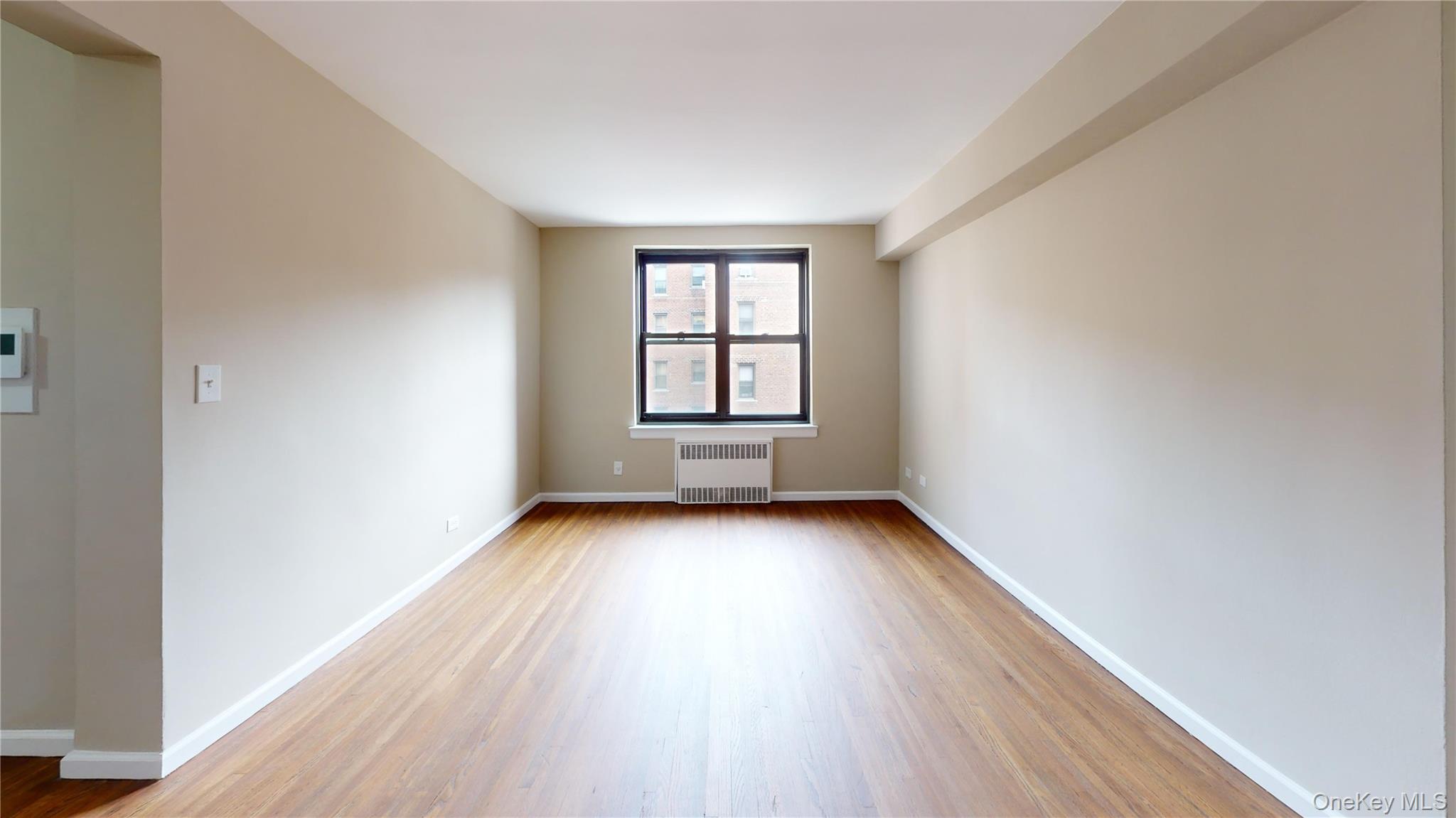112-30 Northern Boulevard, Unit 4B Queens, NY 11368 - Photo 6 of 12 Empty room with wood finished floors and radiator heating unit
