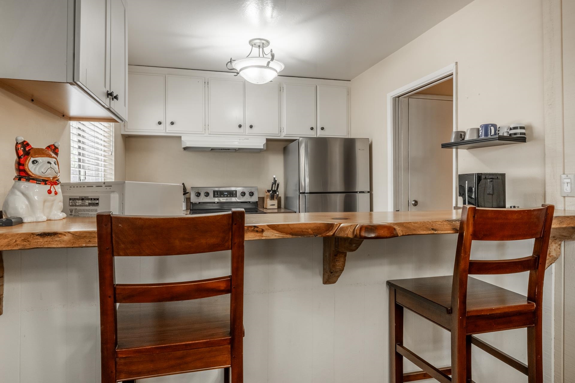 165 Old Mammoth Road, Unit 3 Mammoth Lakes, CA 93546 - Photo 12 of 48 Kitchen featuring a live-edge wood breakfast bar, stainless steel appliances, white cabinetry with dark hardware, and a ceiling-mounted light fixture