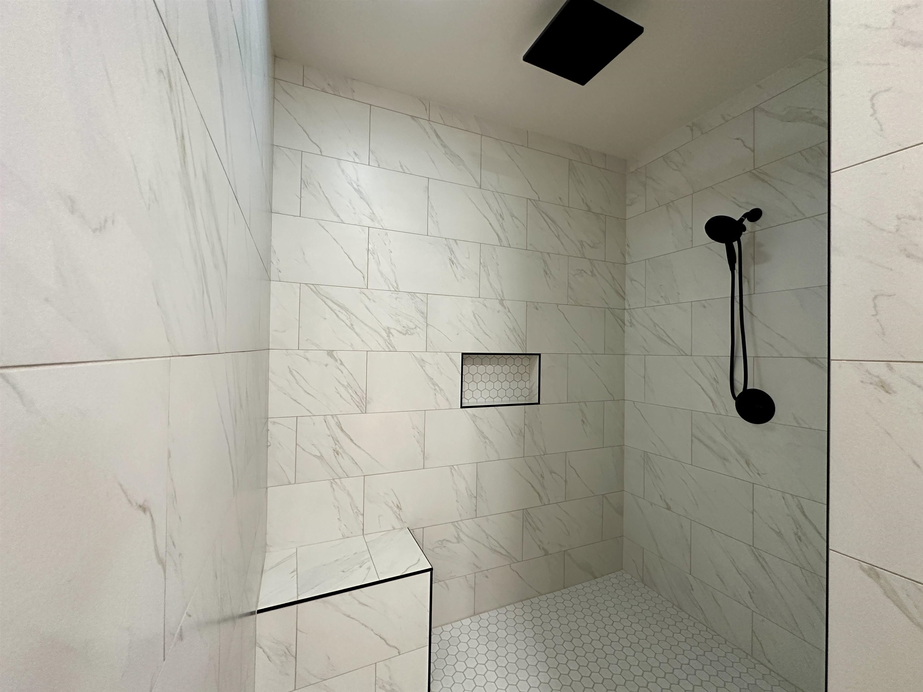 1137 Arl Bailey Road Finger, TN 38334 - Photo 14 of 40 Spacious shower with white rectangular wall tiling, contrasting hexagonal floor tiles, a built-in shower bench, recessed niche with hexagonal tile accent, and matte black fixtures including a rainfall shower head