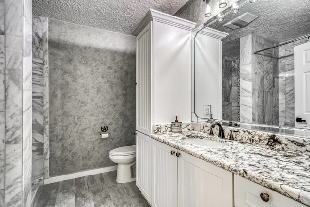 a bathroom with a granite countertop sink a toilet and shower