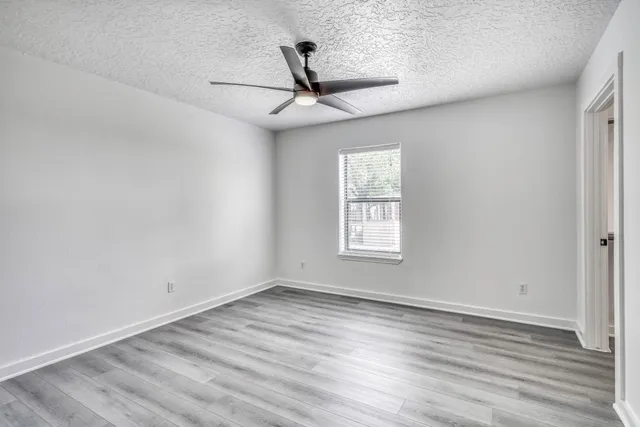 an empty room with wooden floor ceiling fan and windows