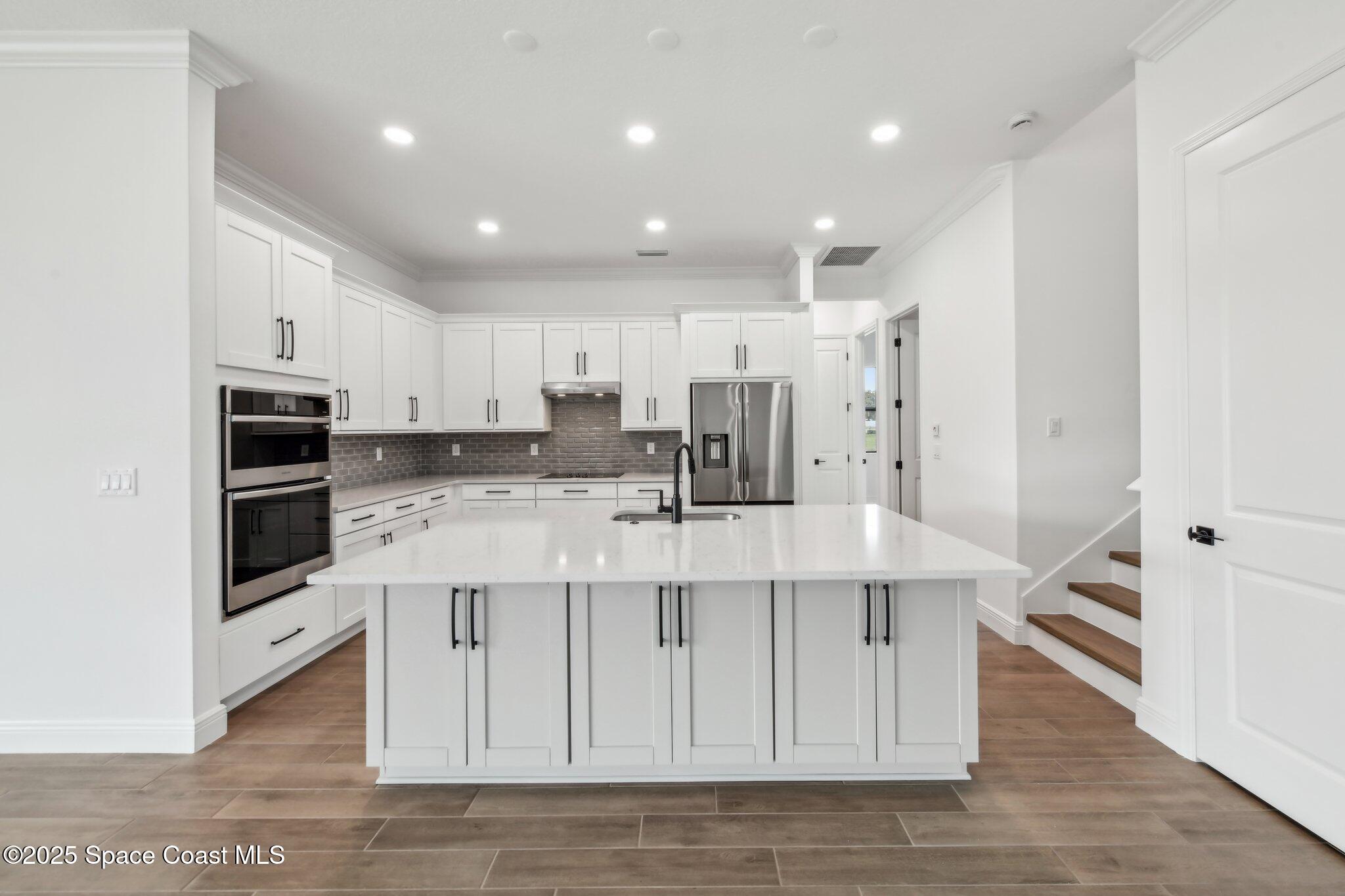 1405 Windchime Lane Melbourne, FL 32935 - Photo 19 of 48 a large white kitchen with stainless steel appliances granite countertop a stove a sink a refrigerator and white cabinets with wooden floor