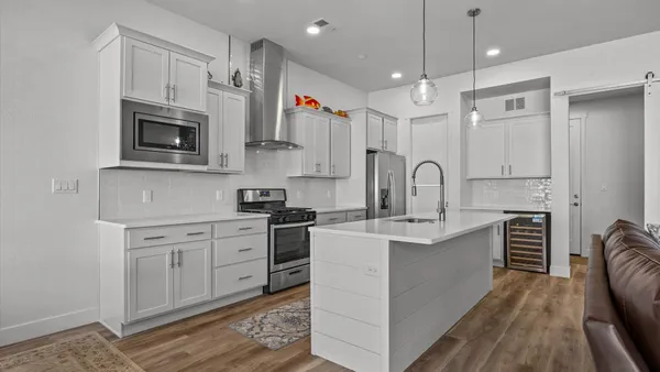 a kitchen with stainless steel appliances granite countertop a stove top oven a sink dishwasher and a refrigerator with wooden floor