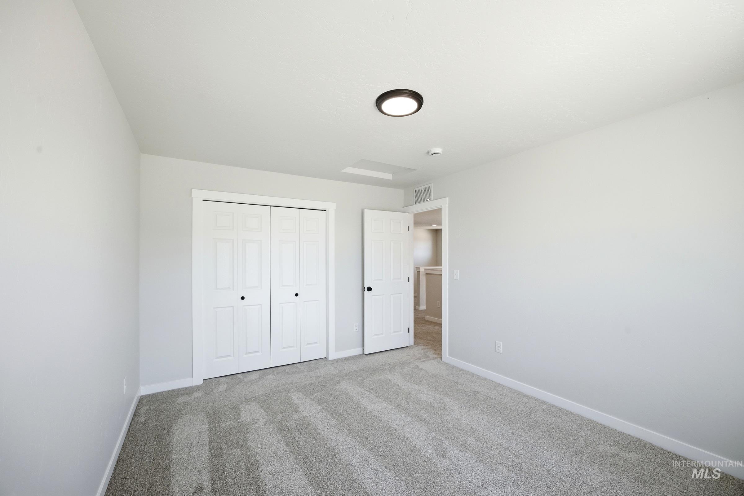 12841 Decatur Street Nampa, ID 83651 - Photo 17 of 30 Neutral-toned room featuring light gray walls, plush carpet flooring, white bi-fold closet doors with black hardware, and a modern flush-mount ceiling light fixture