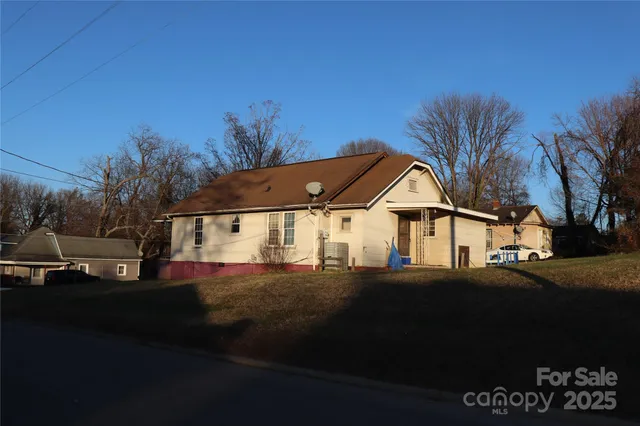 a view of a white house next to a road with big trees