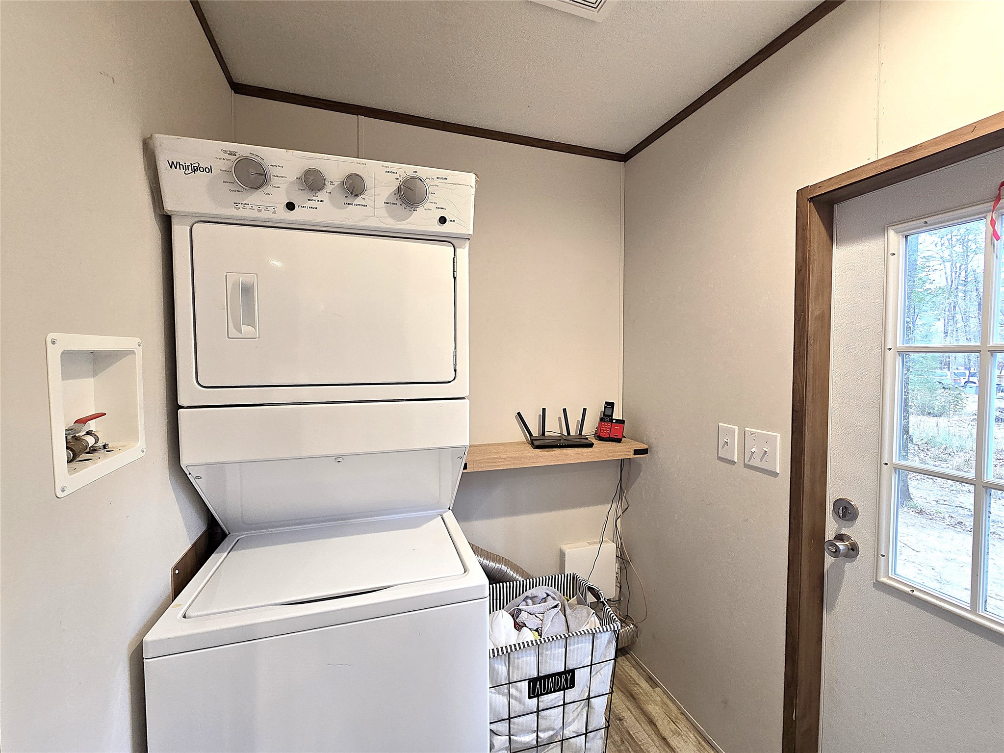 20 Morris Creek Road Coldspring, TX 77331 - Photo 17 of 29 This photo shows a laundry room featuring a stacked washer and dryer unit. It includes a small shelf for storage and a windowed door providing natural light. The room has a clean, functional design with wood-trim accents. Also plenty of room for side by side appliances.