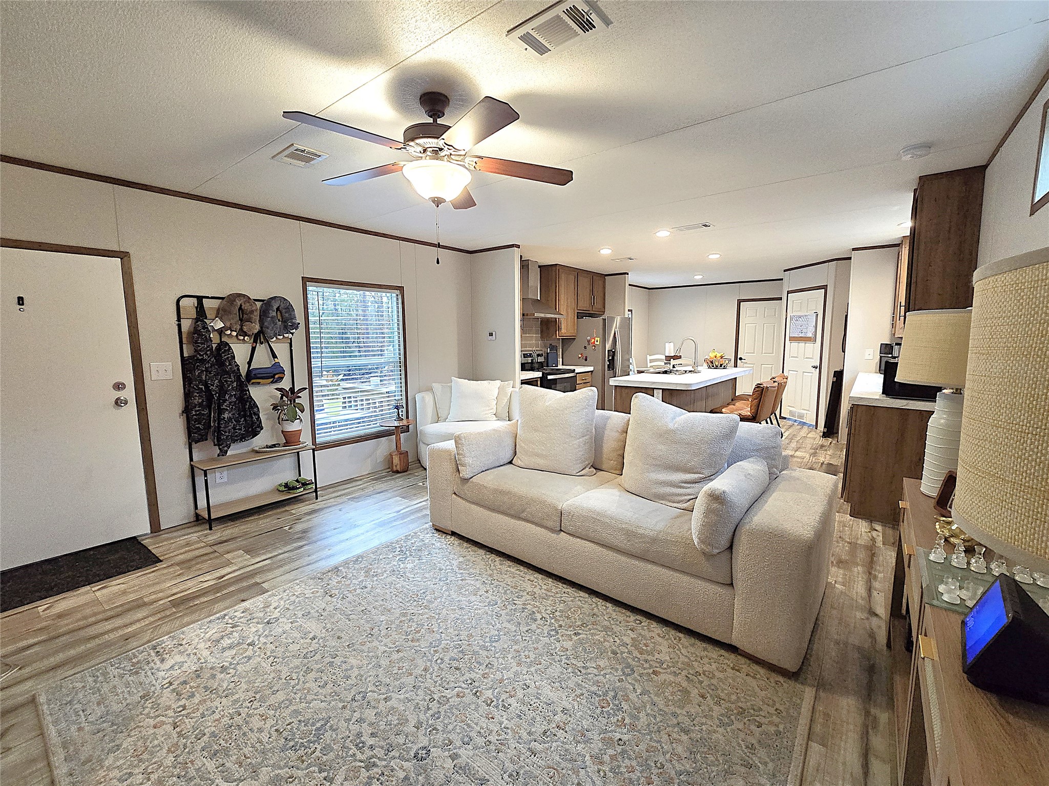 20 Morris Creek Road Coldspring, TX 77331 - Photo 5 of 29 This open-concept kitchen and living area features modern appliances, a central island with seating, and laminate wood flooring. Large windows provide natural light, and the space flows seamlessly into a cozy living room with a ceiling fan and a large TV. Perfect for entertaining and family gatherings.