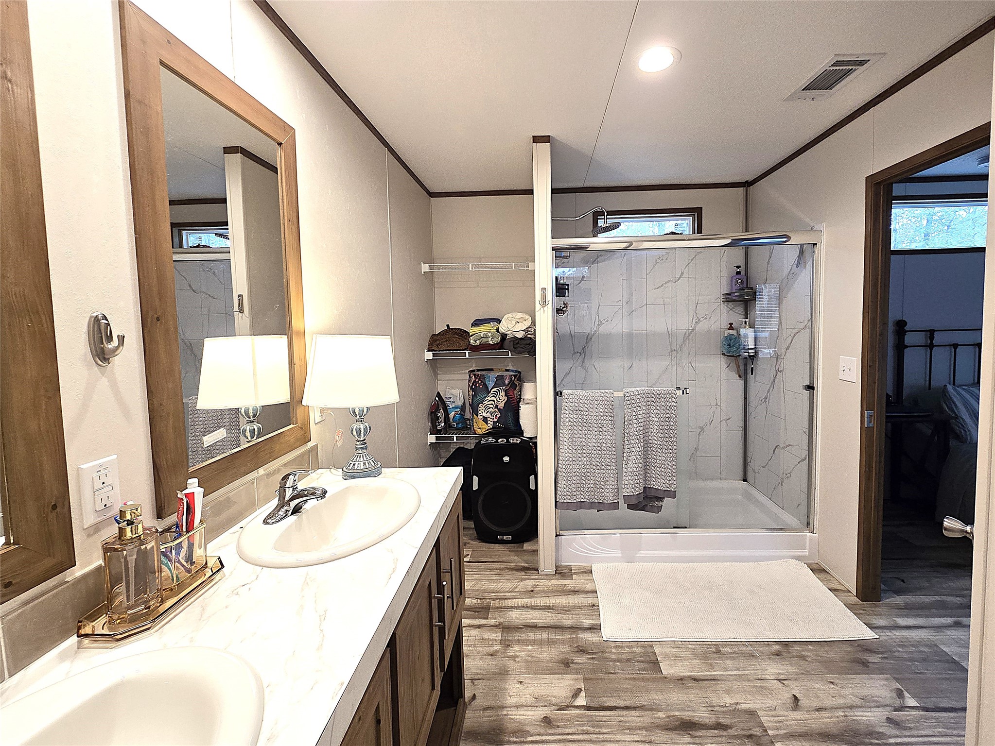 20 Morris Creek Road Coldspring, TX 77331 - Photo 7 of 29 This bathroom features a modern design with dual sinks and wooden cabinetry. It has a spacious glass-enclosed shower, elegant mirrors, and stylish wood-look flooring, providing a warm and inviting atmosphere.