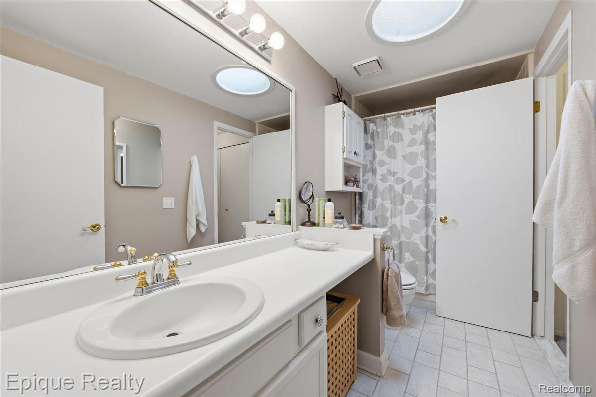 26 Kirks Court Rochester, MI 48309 - Photo 25 of 44 Bathroom vanity with an integrated sink and gold-tone faucet, featuring a large mirror and overhead lighting