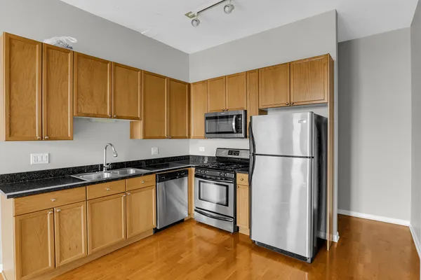 a kitchen with stainless steel appliances granite countertop a refrigerator a sink dishwasher and wooden cabinets with wooden floor