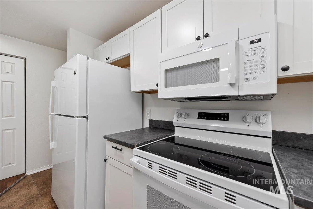 259 Pheasant Road, Unit 84 Twin Falls, ID 83301 - Photo 10 of 25 Kitchen featuring white cabinetry, dark countertops, a white electric range with a smooth cooktop, a built-in microwave, and a white refrigerator