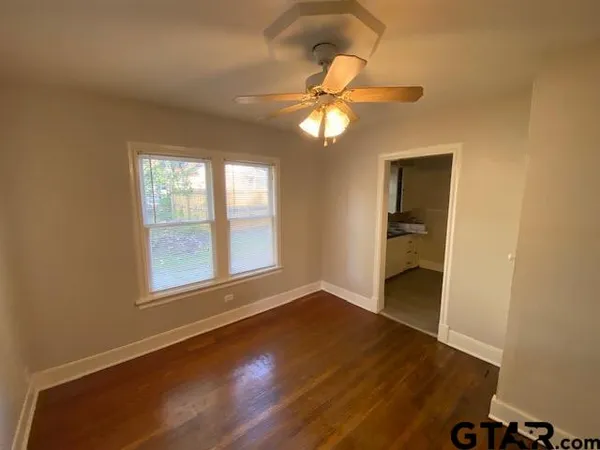 an empty room with wooden floor fan and windows