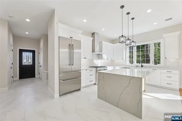 a large kitchen with stainless steel appliances kitchen island granite countertop a refrigerator a sink dishwasher a stove and white cabinets with wooden floor