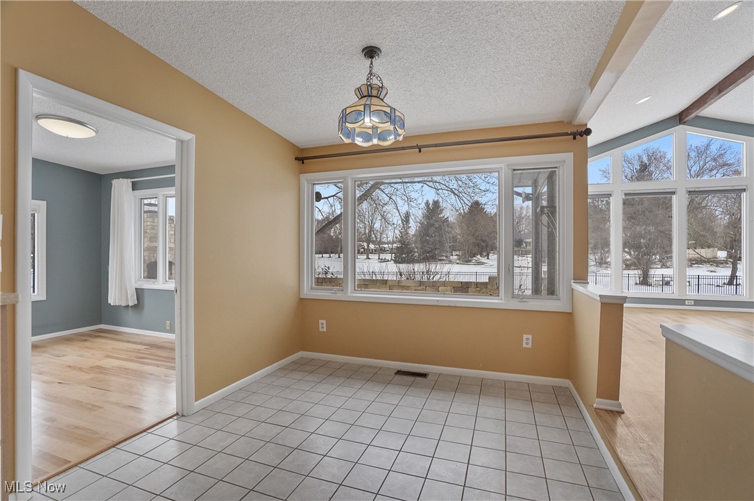 1094 San Raphael Drive Akron, OH 44333 - Photo 16 of 50 Unfurnished dining area featuring light tile patterned floors, a chandelier, a textured ceiling, and beam ceiling