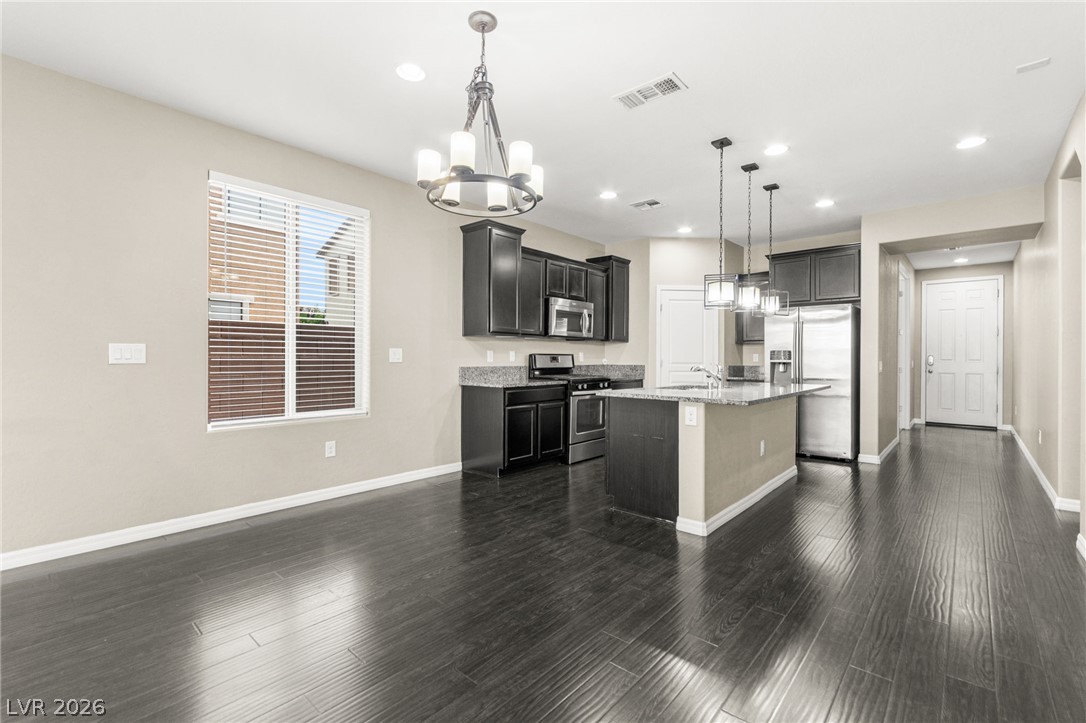 11048 Prairie Grove Road Las Vegas, NV 89179 - Photo 19 of 75 Rich hardwood flooring leads to a spacious kitchen featuring dark cabinetry and a central island.