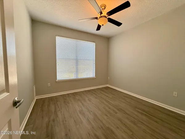 an empty room with wooden floor fan and windows
